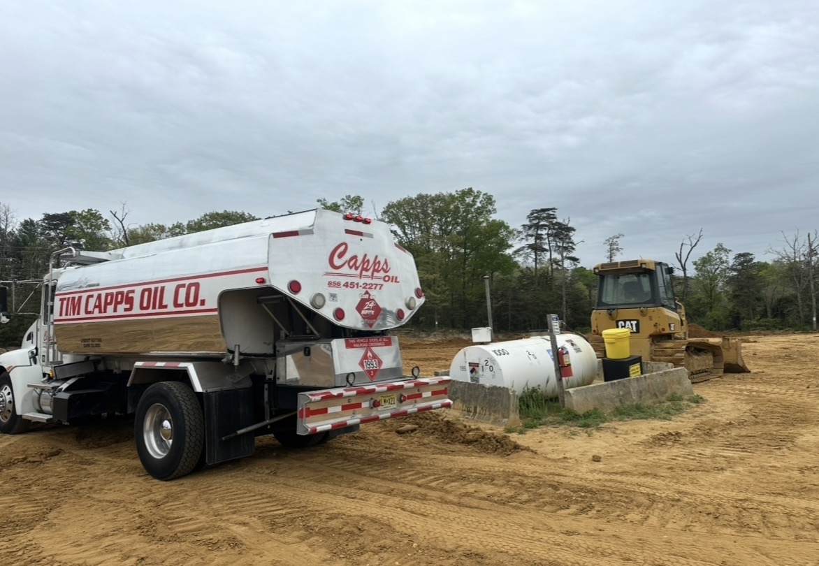 Tim Capps Oil Co. tanker delivering fuel next to a CAT dozer and storage tank